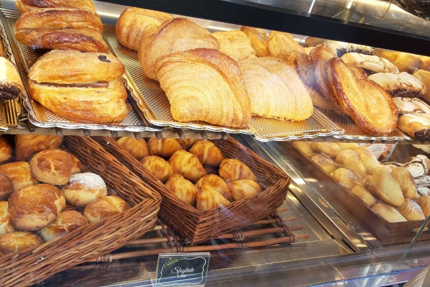 An assortment of baked goods including croissants, pastries, and bread in a bakery display case. 1