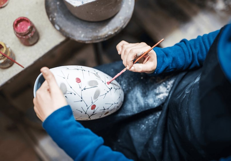 A person painting a ceramic bowl with a floral pattern. 1