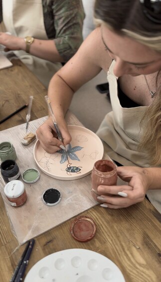 A person painting on a ceramic plate with various paint colors around. 2