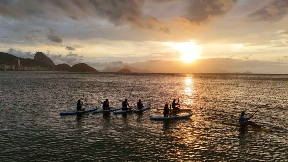 A group of people paddleboarding on a calm sea during sunset. 1