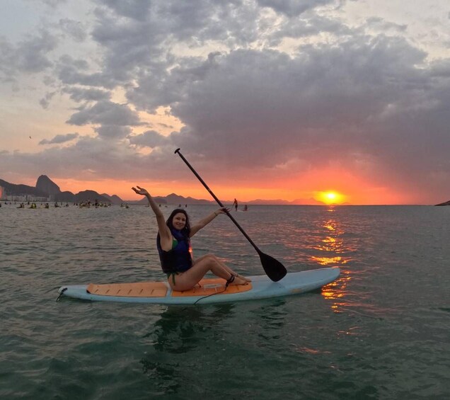 A person sitting on a paddleboard in the ocean with a sunset in the background. 3