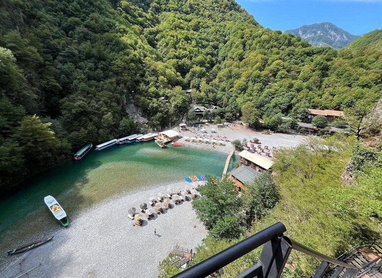 A coastal area with a boat dock, a beach with umbrellas, and a forested hillside. 3
