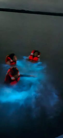 Three people in red life jackets floating on a body of water. 4