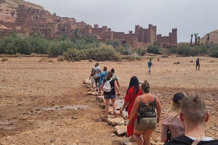 A group of people walking on a rocky path in a desert landscape with traditional buildings in the background. 4