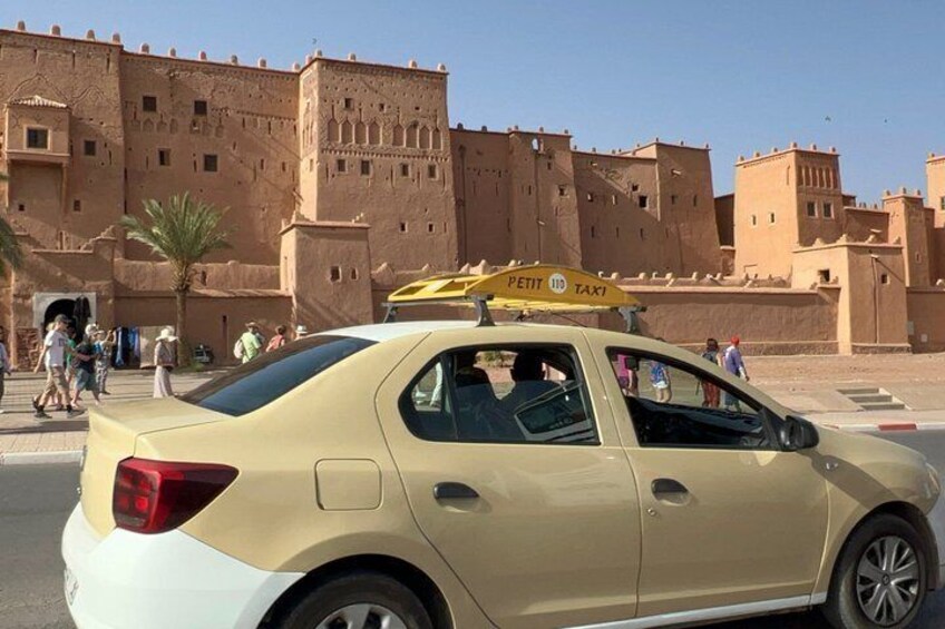 A yellow taxi with a sign in front of a large, historic building. 2