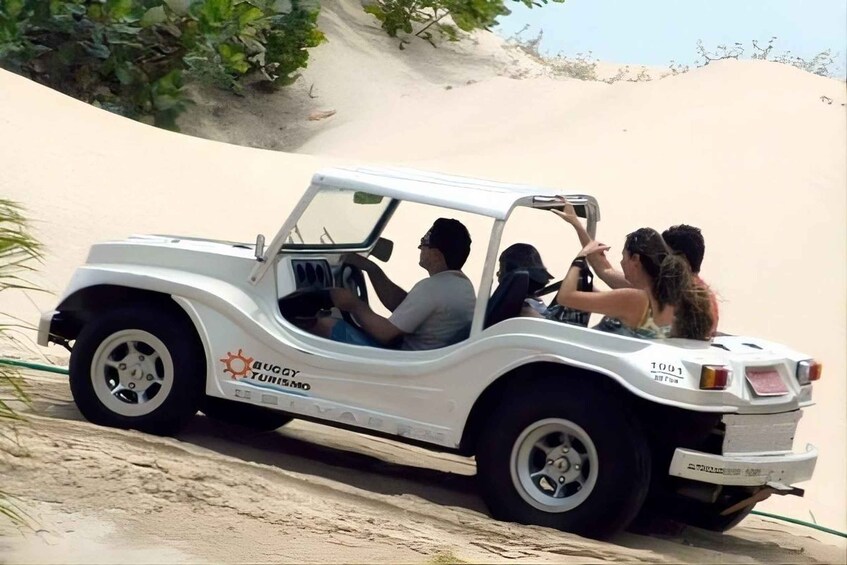 A white dune buggy with 'Dune Tour' branding, driving on a sandy dune. 3