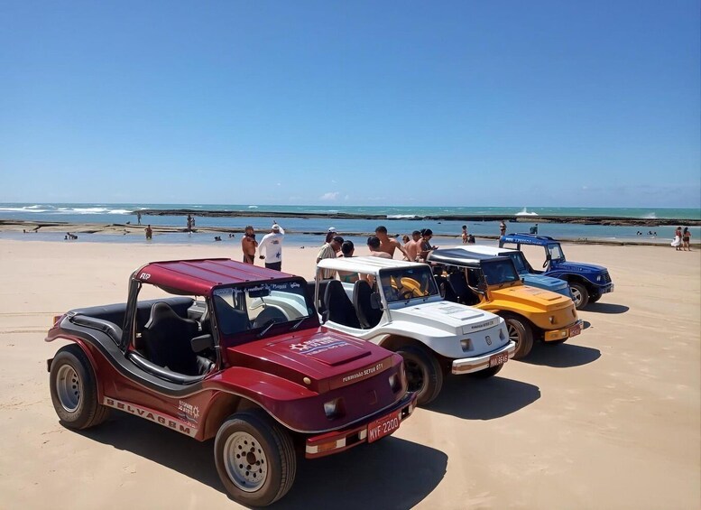 A row of off-road vehicles parked on a sandy beach with people in the background. 1