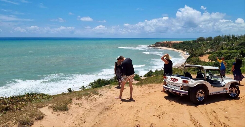 A beach with a dune, ocean, and a vehicle. 4