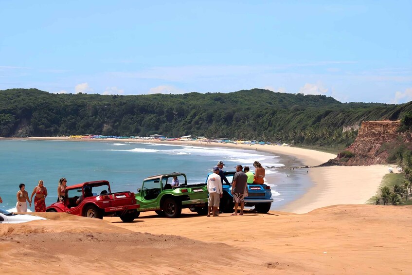A beach with a dune, a jeep, and people. 2