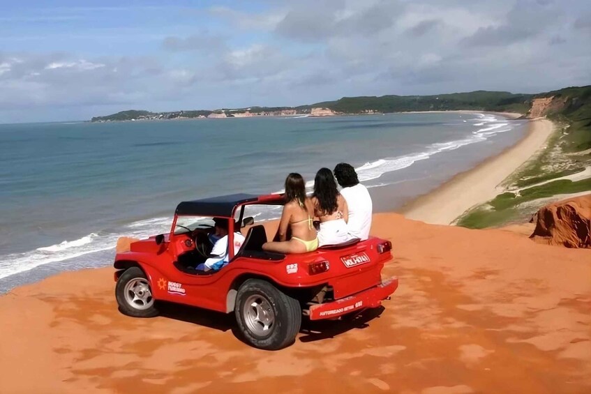A red off-road vehicle on a sandy beach with the ocean in the background. 2