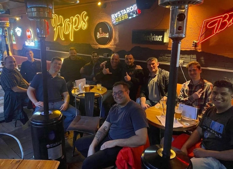 A group of people seated at tables in a bar with neon signs and a beer tap. 1