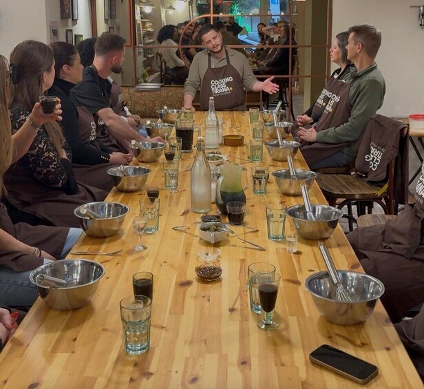 A group of people around a long table with cooking utensils and glasses, likely participating in a cooking class. 4