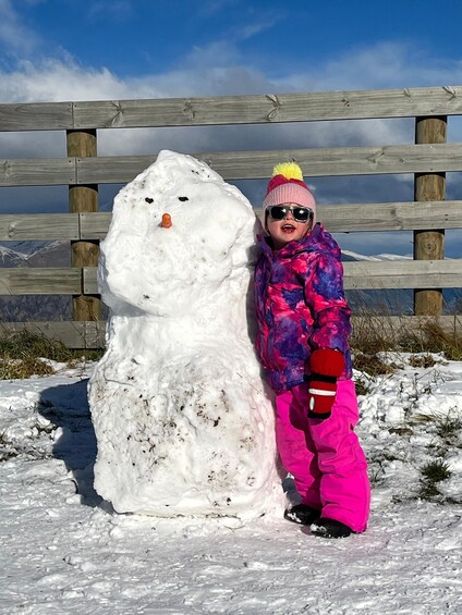 A child in a colorful outfit next to a snowman in a snowy outdoor setting. 2