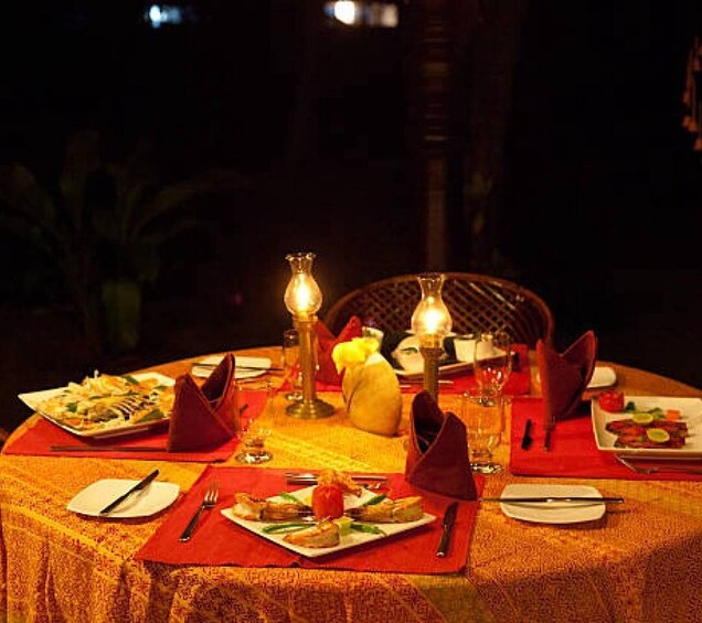 An outdoor dining table set with plates of food, red napkins, and candles. 3