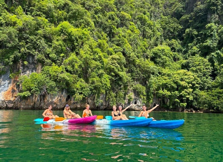 A group of people in colorful kayaks on a calm river, surrounded by lush green forest and rocky cliffs. 1