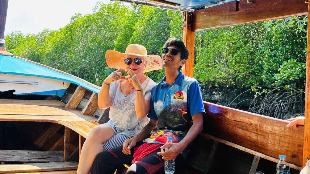 Two people sitting on a wooden boat docked near mangrove trees. 4