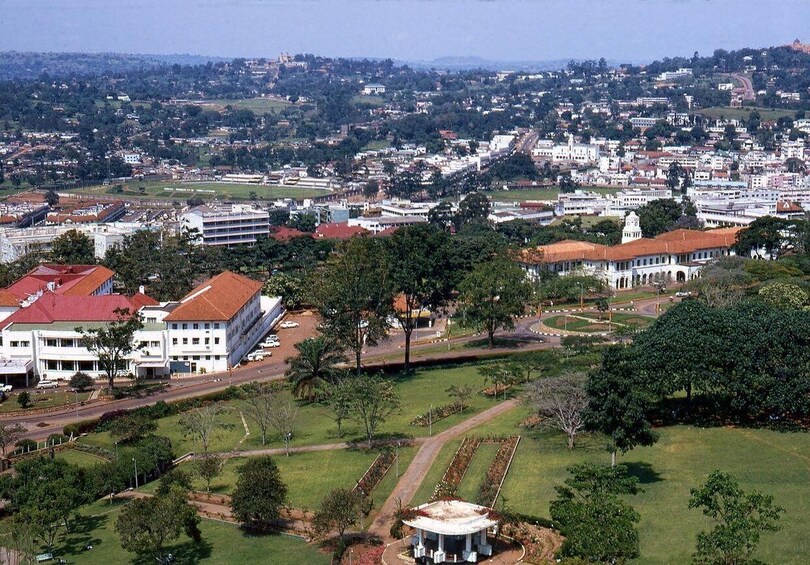 A cityscape with a prominent white building with a red roof, a large green park area, and a distant hill with scattered buildings. 3