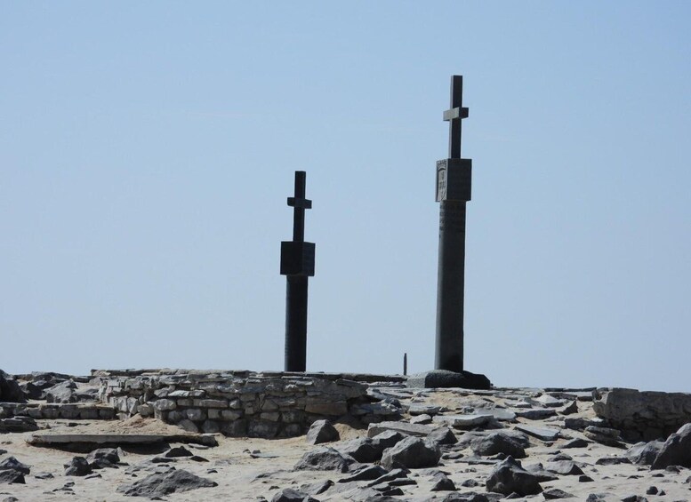 Two tall, dark crosses on a rocky, historical site with stone ruins in the background. 1