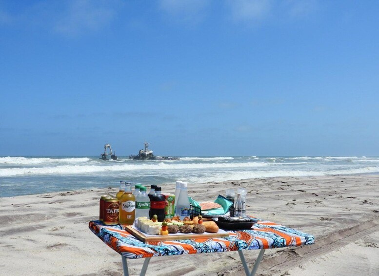 A beach with a table set for a meal, bottles, and a chair. 4