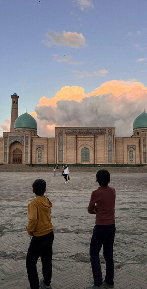 A large mosque with two green domes and a tall minaret, surrounded by a paved courtyard. 1