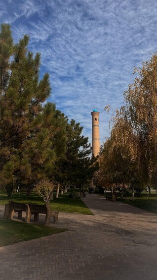 A park with a tall tower, benches, and trees. 2