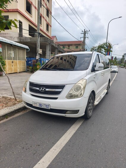 A white van parked on a city street with buildings and power lines in the background. 3