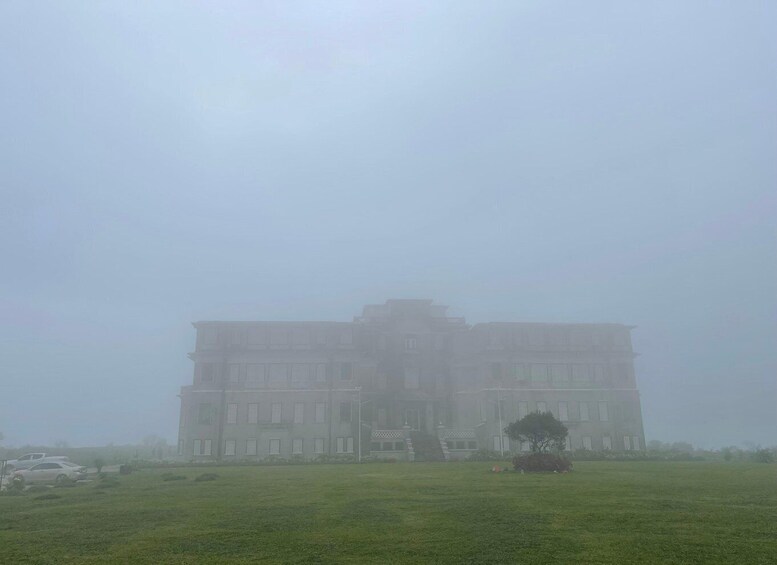 A large building with multiple stories, surrounded by a grassy field and a few trees. 5