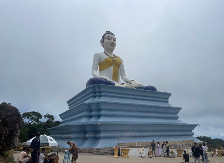 A large seated Buddha statue on a multi-tiered pedestal with people around it. 4