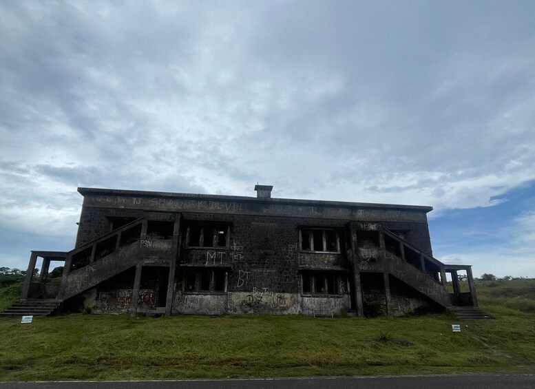 A dilapidated building with graffiti, surrounded by grass and a cloudy sky. 1