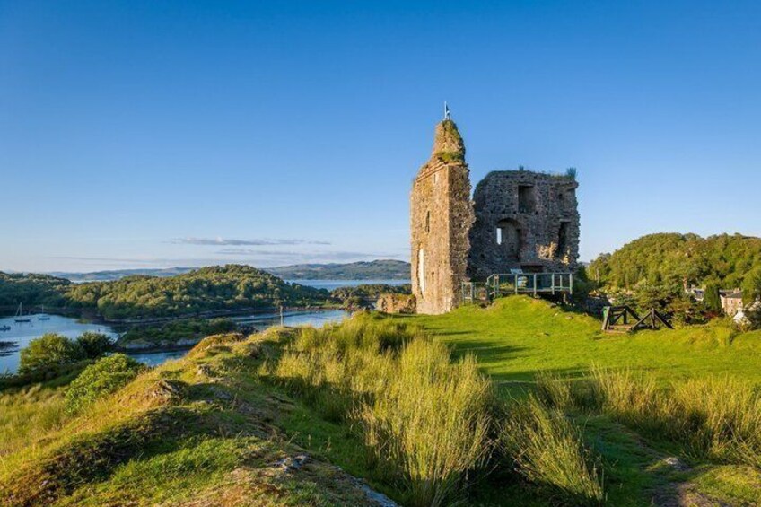 A historic stone tower and ruins on a grassy hill overlooking a river. 1