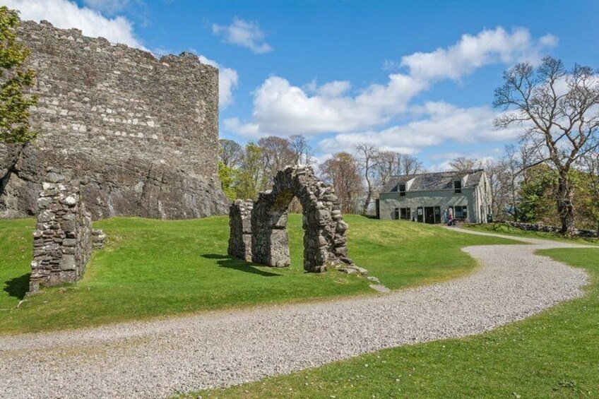A historic stone structure, a grassy pathway, and a building in the background. 2