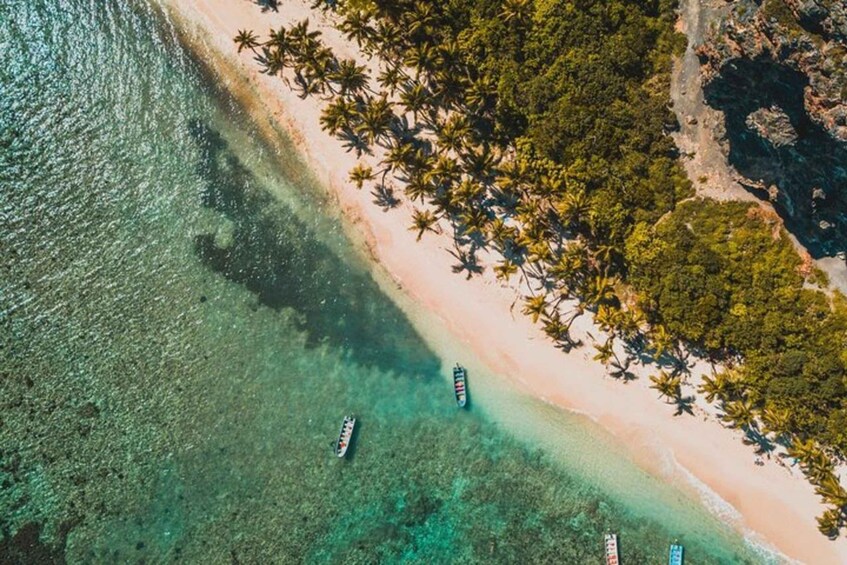 An aerial view of a beach with clear turquoise water, palm trees, and a few boats. 3