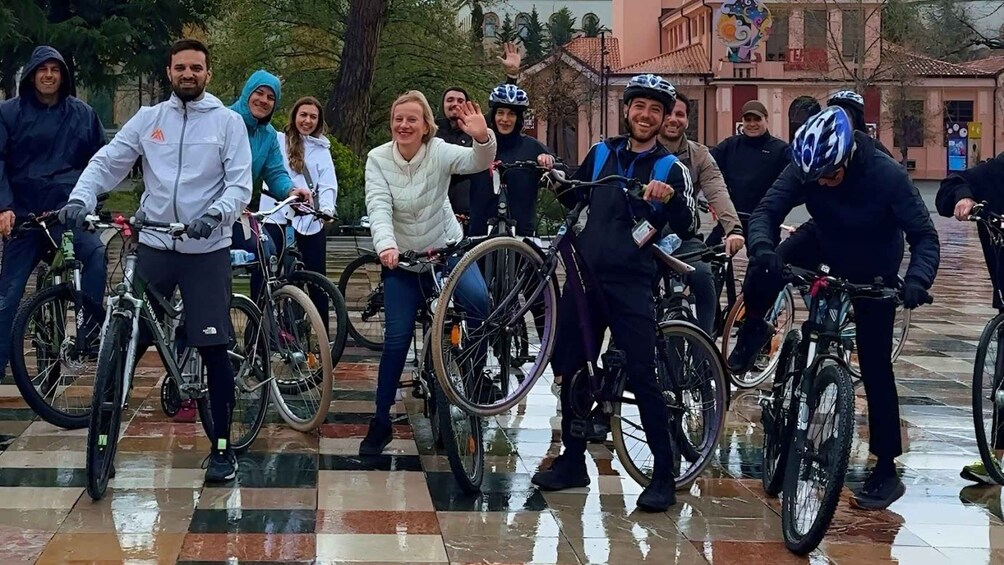 A group of cyclists in a wet urban setting with tiled pavement and buildings in the background. 4