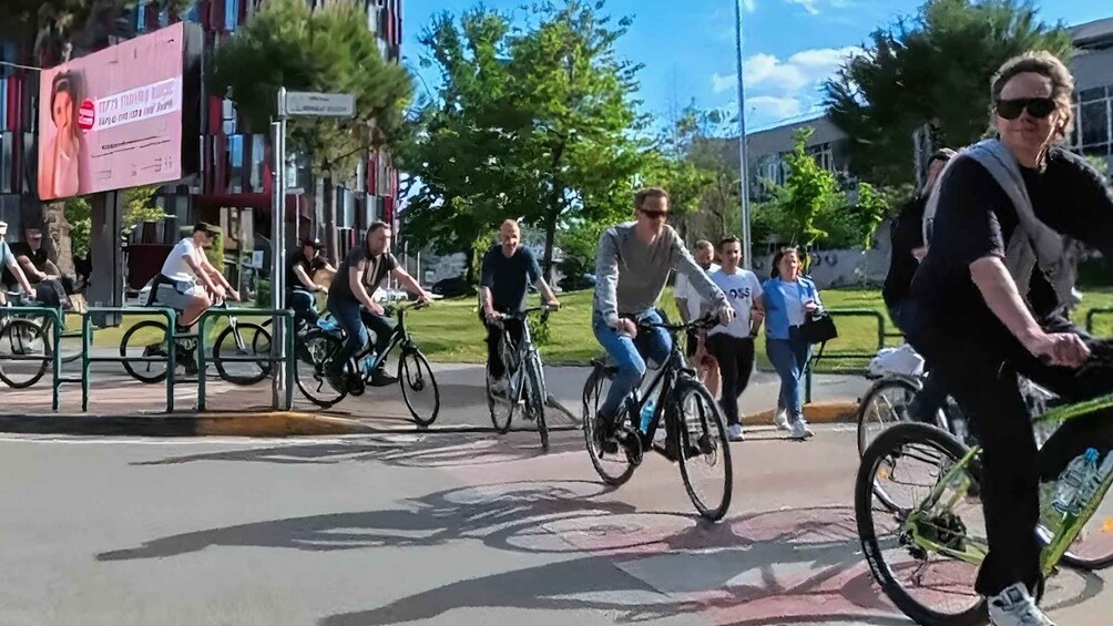People riding bicycles on a street with trees and a building in the background. 3