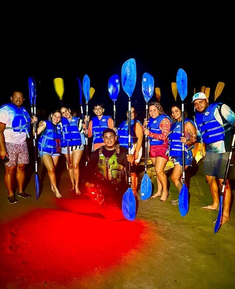 A group of people in blue life vests holding paddles, standing on a red surface at night. 1