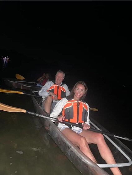 Two people in a canoe wearing life jackets, paddling on a body of water at night. 2