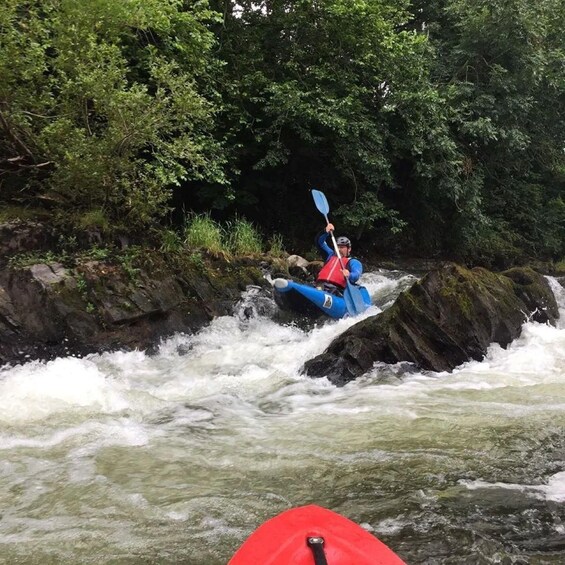 A person kayaking down a river with rapids, surrounded by lush greenery. 3