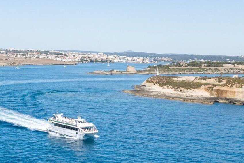 A white boat traveling on a blue sea with a coastal town in the background. 1