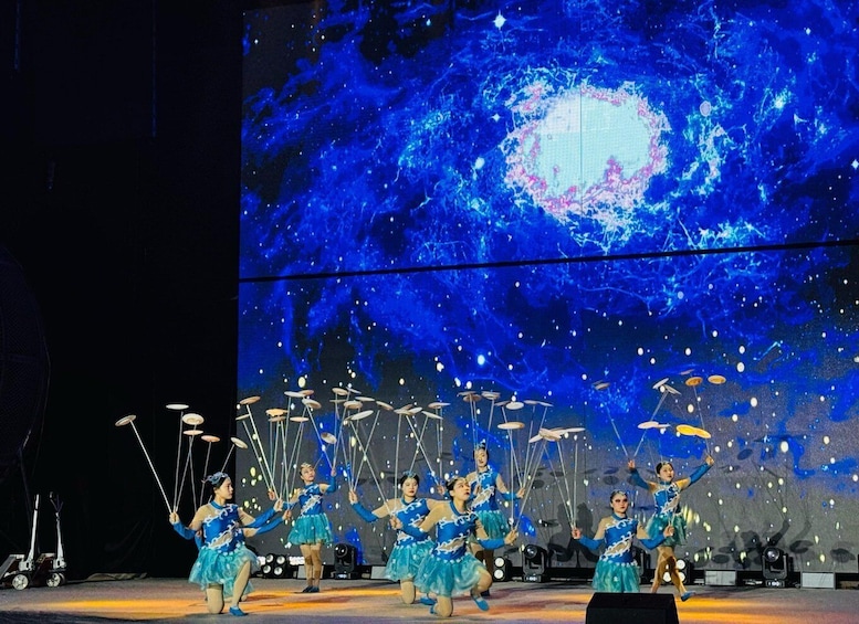A group of performers in blue costumes with a cosmic-themed backdrop. 5