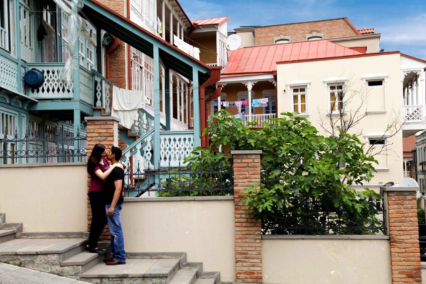 A couple kissing on a staircase in a residential area with colorful buildings and a tree. 1