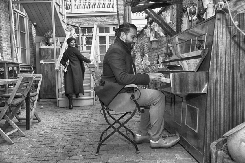 A man playing a piano in an outdoor setting with brick walls and wooden furniture. 2