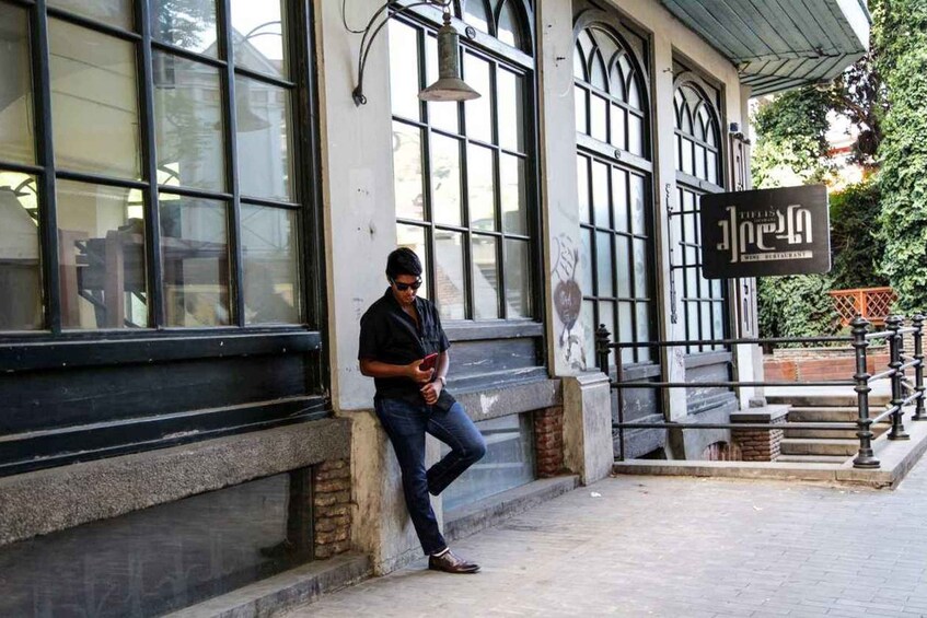 A person leaning on a building's exterior wall, a sign reading 'Wine Restaurant' above a staircase, and a street lamp. 5