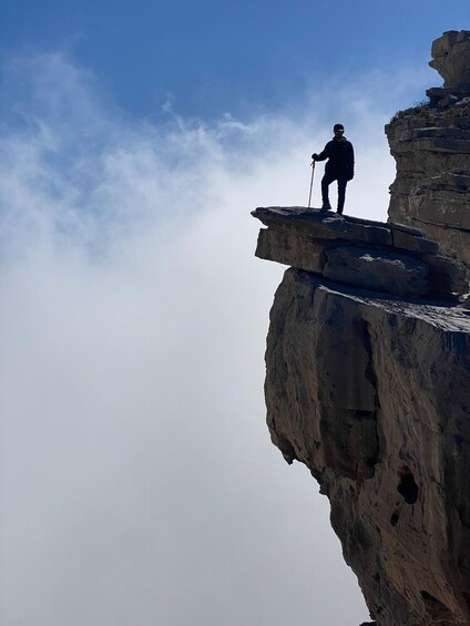 A person standing on a rock ledge with a walking stick, overlooking a cliff. 2