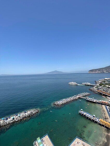 A coastal town with clear waters, a pier, and a mountain in the distance. 1