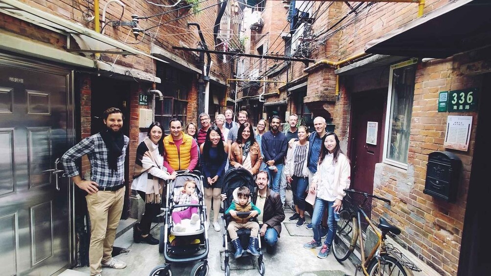 A group of people in a narrow alleyway with brick buildings, a bicycle, and a stroller. 1
