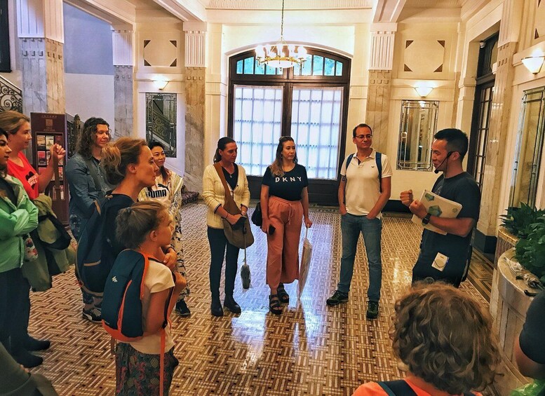 A group of people standing in a lobby with a patterned floor and a large arched doorway. 4