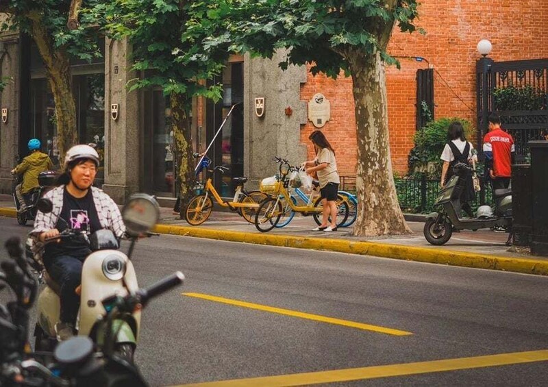 A street scene with a person riding a scooter, a bicycle, and a person walking. 3
