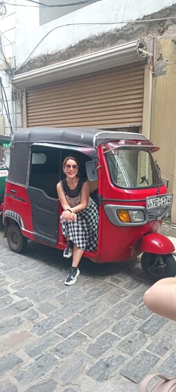 A woman sitting on a red auto-rickshaw parked on a cobblestone street. 1