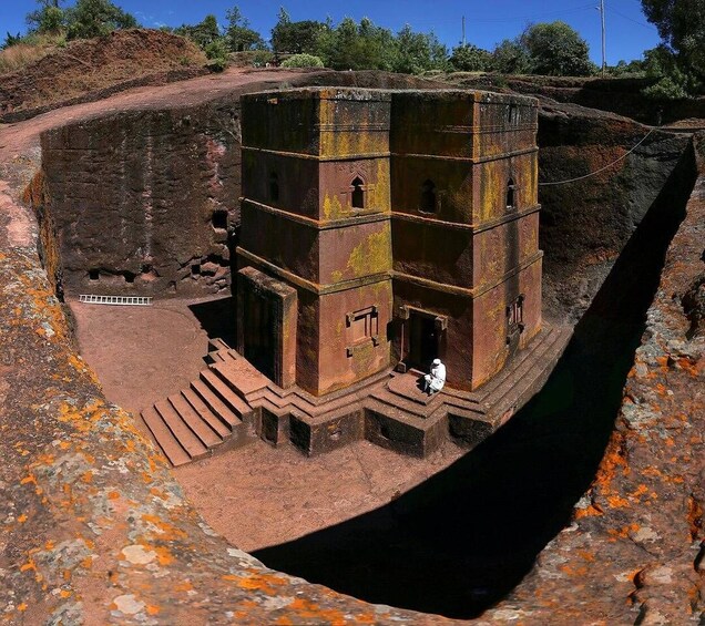 Une structure ancienne à plusieurs niveaux, dotée d’un escalier menant à une porte, le tout étant entouré d’un paysage rocheux. 1