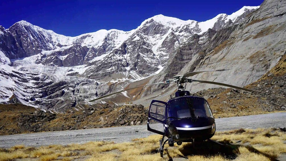 A helicopter parked on a road with snow-capped mountains in the background. 1